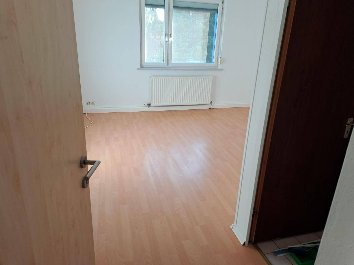 Geräumiges Zimmer mit Laminatboden und einem Fenster, gesehen durch eine offene Holztür.