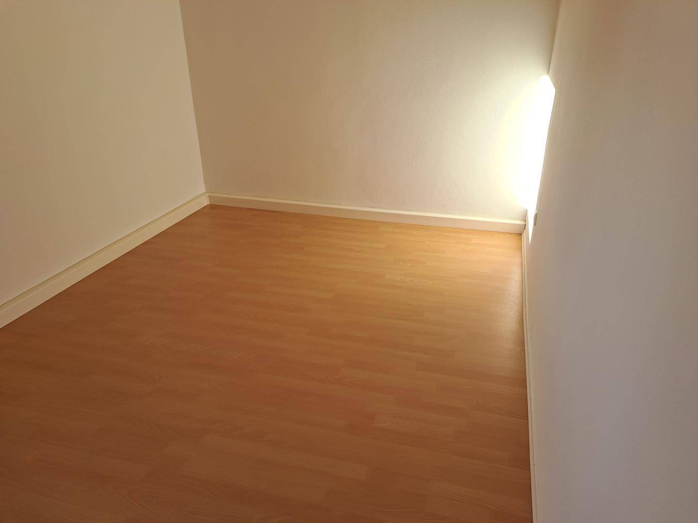 Helles, leeres Zimmer mit Laminatboden und natürlichem Lichteinfall durch ein seitliches Fenster.