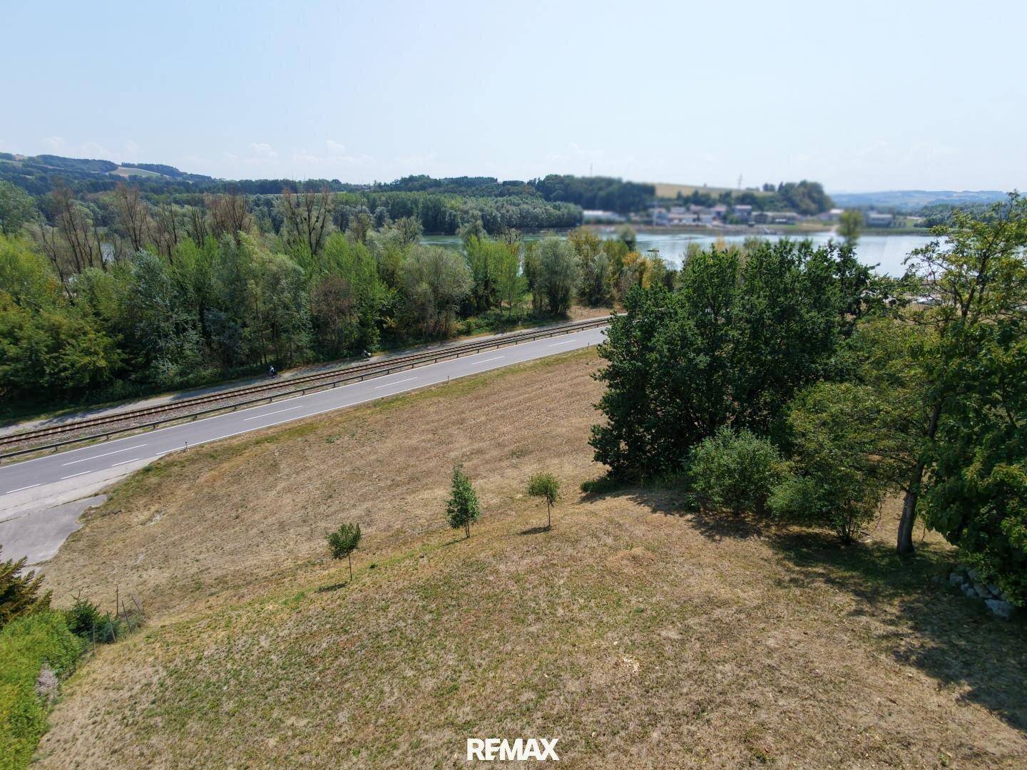 Weitläufige Landschaftsaufnahme mit Fluss, Straße und bewaldeten Ufern unter blauem Himmel.