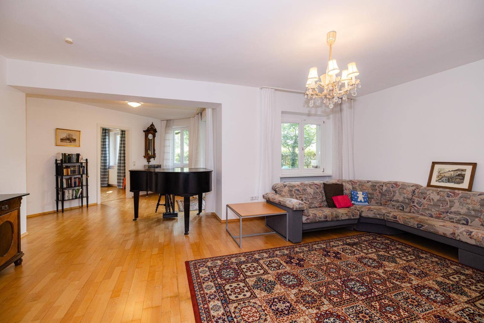 Geräumiges Wohnzimmer mit hellem Parkettboden, einem Flügel und einem gemütlichen Sofa.