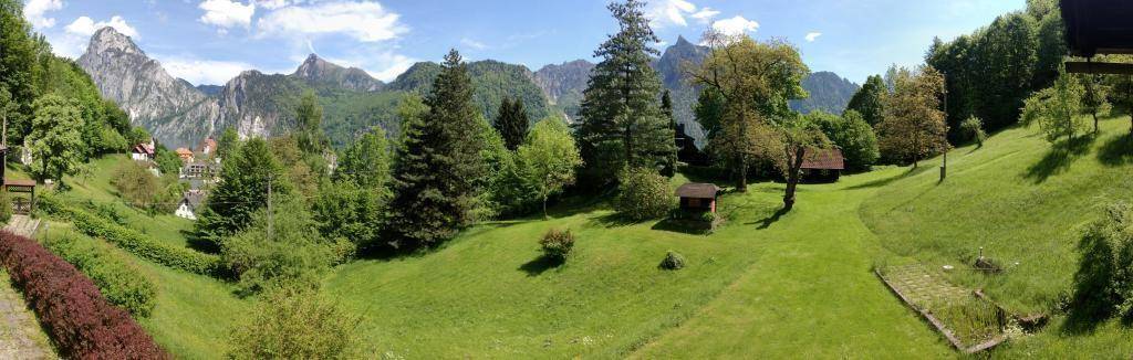 Weitläufige grüne Landschaft mit sanften Hügeln, Bäumen und imposanten Bergen unter klarem Himmel.