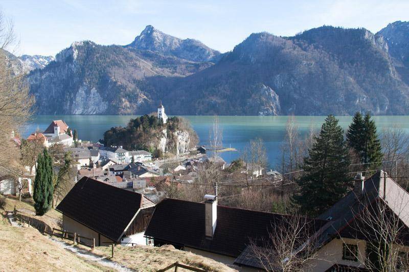 Panoramablick auf eine charmante Stadt am Seeufer mit einer Kirche auf einer Insel und hohen Bergen.