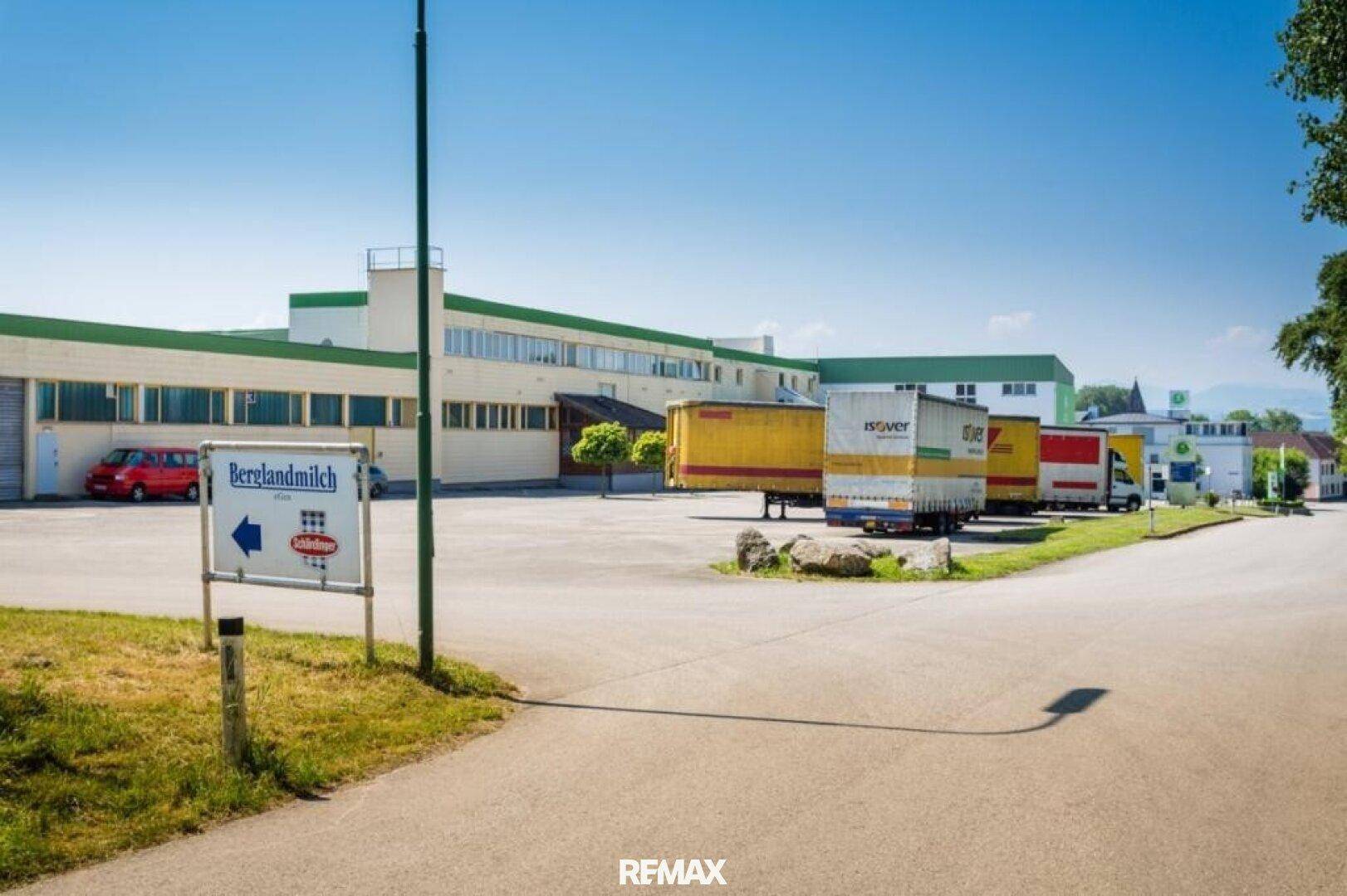 Weitläufige Außenansicht eines Gewerbekomplexes mit LKW-Parkplätzen und Zufahrtsstraße unter blauem Himmel.