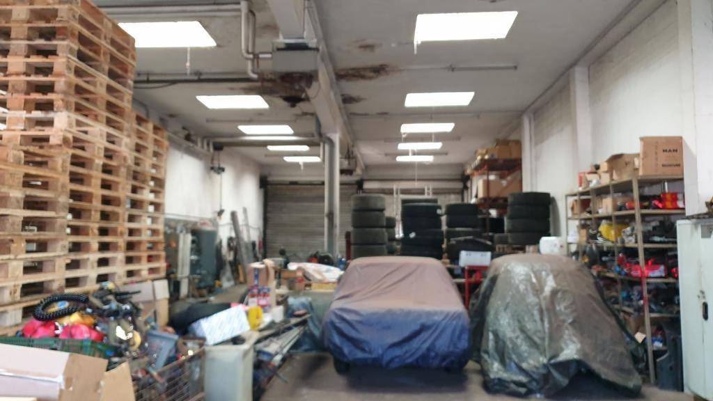 Blick in eine Werkstatt oder Lagerhalle mit gestapelten Paletten, Reifen und abgedeckten Gegenständen.
