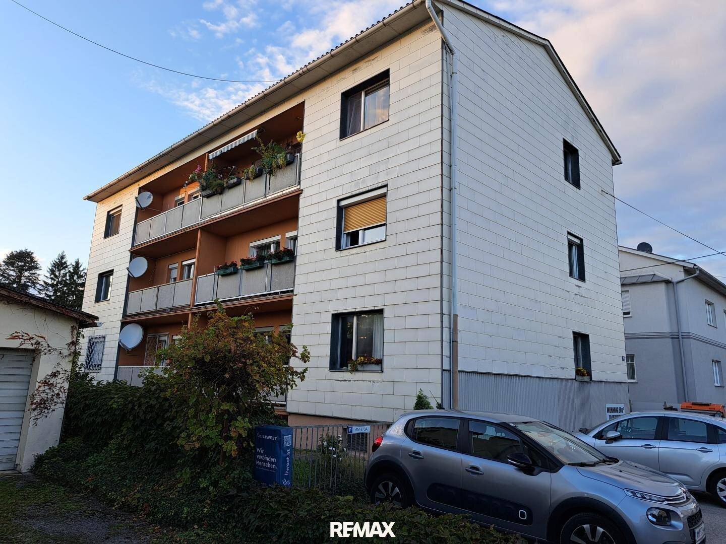 Mehrfamilienhaus mit mehreren Balkonen und weißer Fassadenverkleidung unter blauem Himmel.