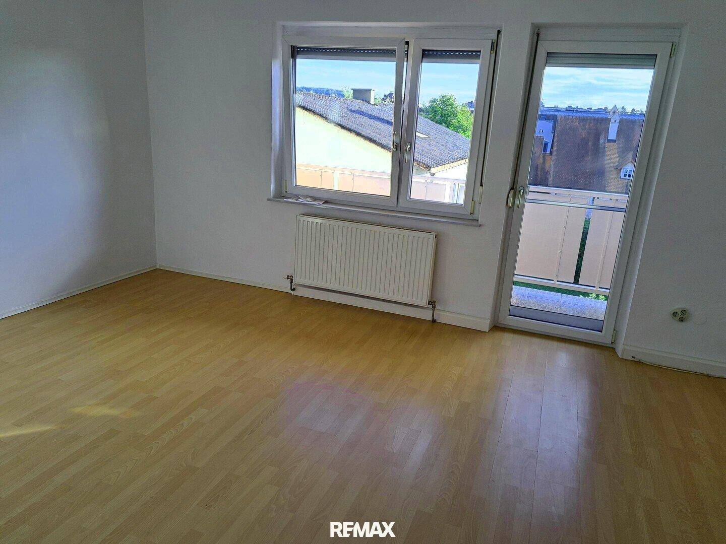 Leeres Schlafzimmer mit Laminatboden, großem Fenster und Zugang zum Balkon.
