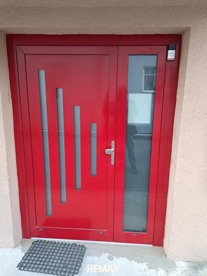 Moderne rote Eingangstür mit vertikalen Glaseinsätzen und seitlichem Fenster.