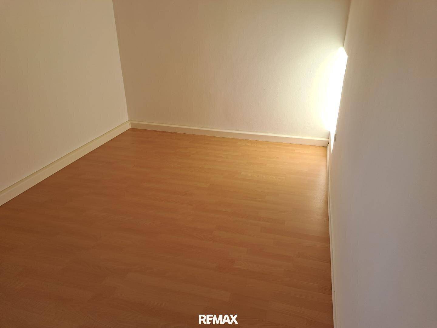 Heller, leerer Raum mit Laminatboden und natürlichem Lichteinfall durch ein Fenster.