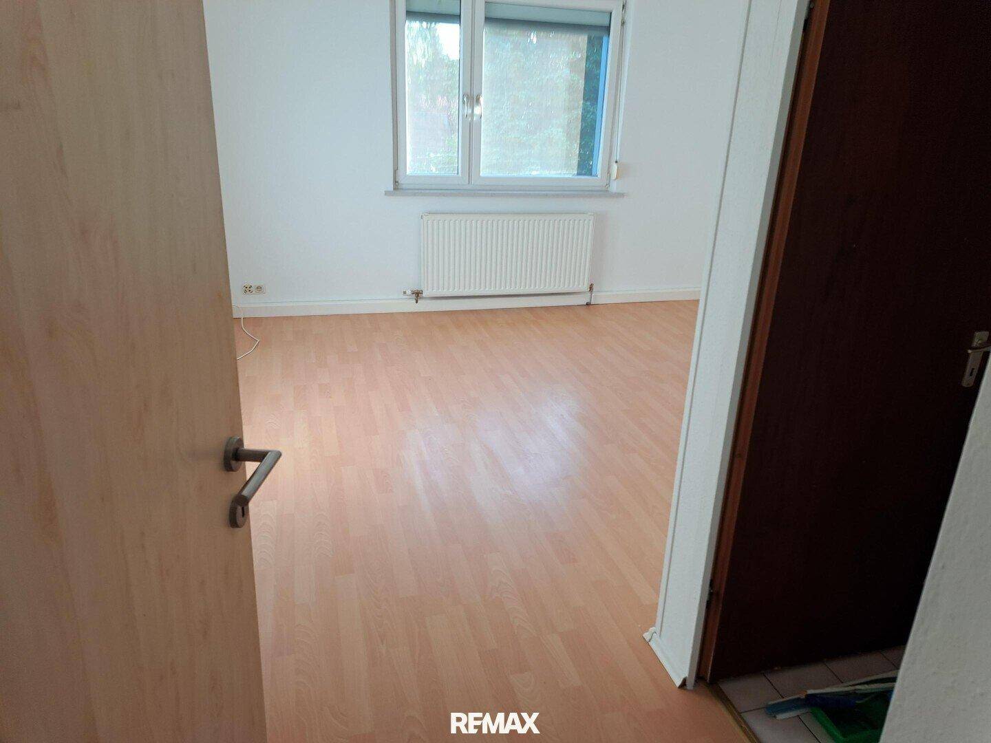 Leeres Zimmer mit Laminatboden, Fenster und einem angenehmen Blick ins Grüne.