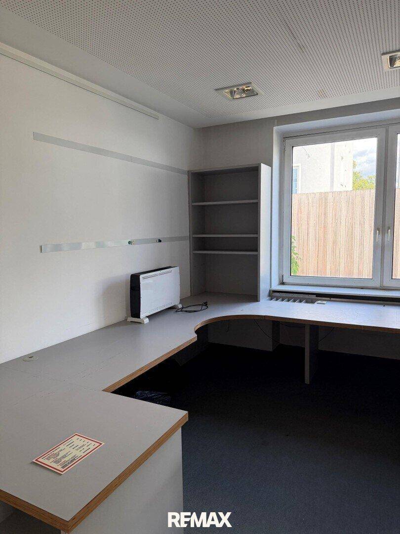 Helles Büro mit großem Schreibtisch, Regal und Fenster mit Blick ins Grüne.