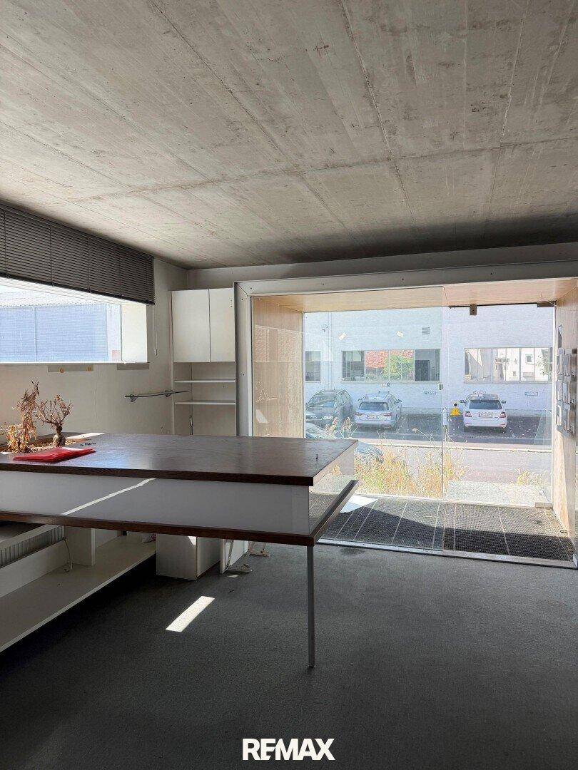 Heller Innenraum mit großer Glasfront und Blick auf den Außenbereich mit Parkplätzen.
