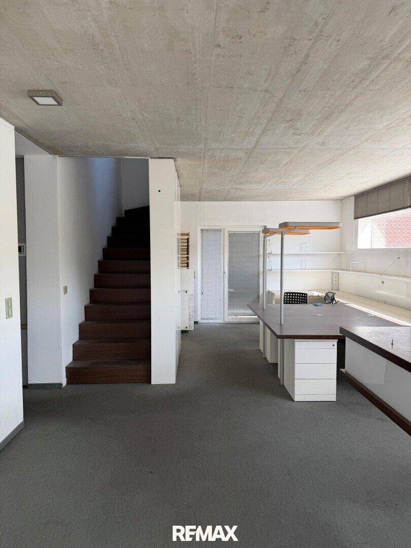 Geräumiger Innenraum mit Holztreppe, offenem Grundriss und Sichtbetondecke.