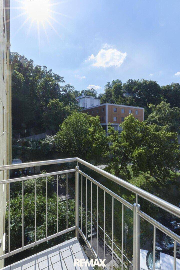 Sonniger Balkon mit Metallgeländer und einem schönen Blick auf grüne Bäume und umliegende Gebäude.