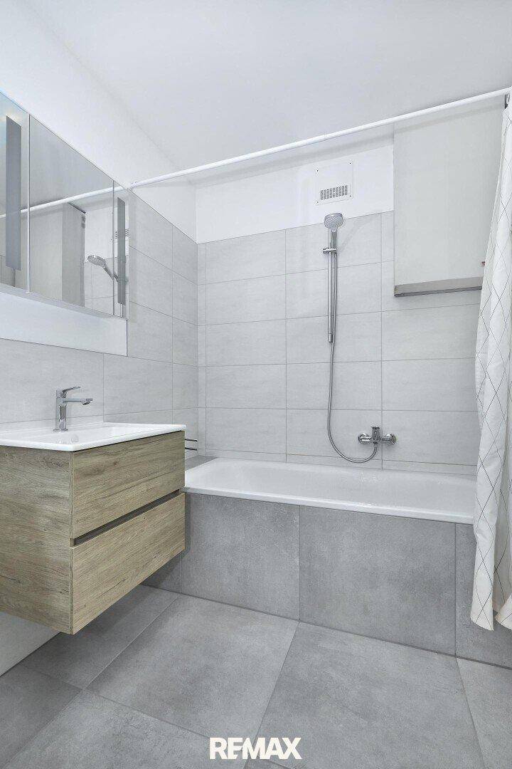 Modernes Badezimmer mit Badewanne, schwebendem Waschtisch und hellgrauen Fliesen.