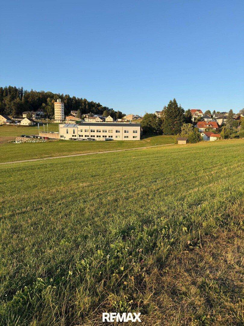Weitläufige Landschaft mit Blick auf ein modernes Gebäude und einen Wasserturm in ländlicher Umgebung.