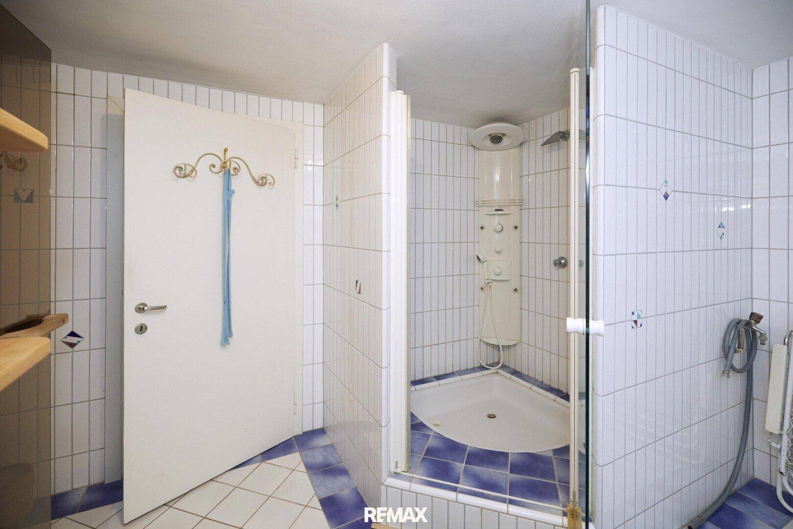 Badezimmer mit Duschkabine, weißen und blauen Fliesen im Retro-Stil und einfacher Ausstattung.