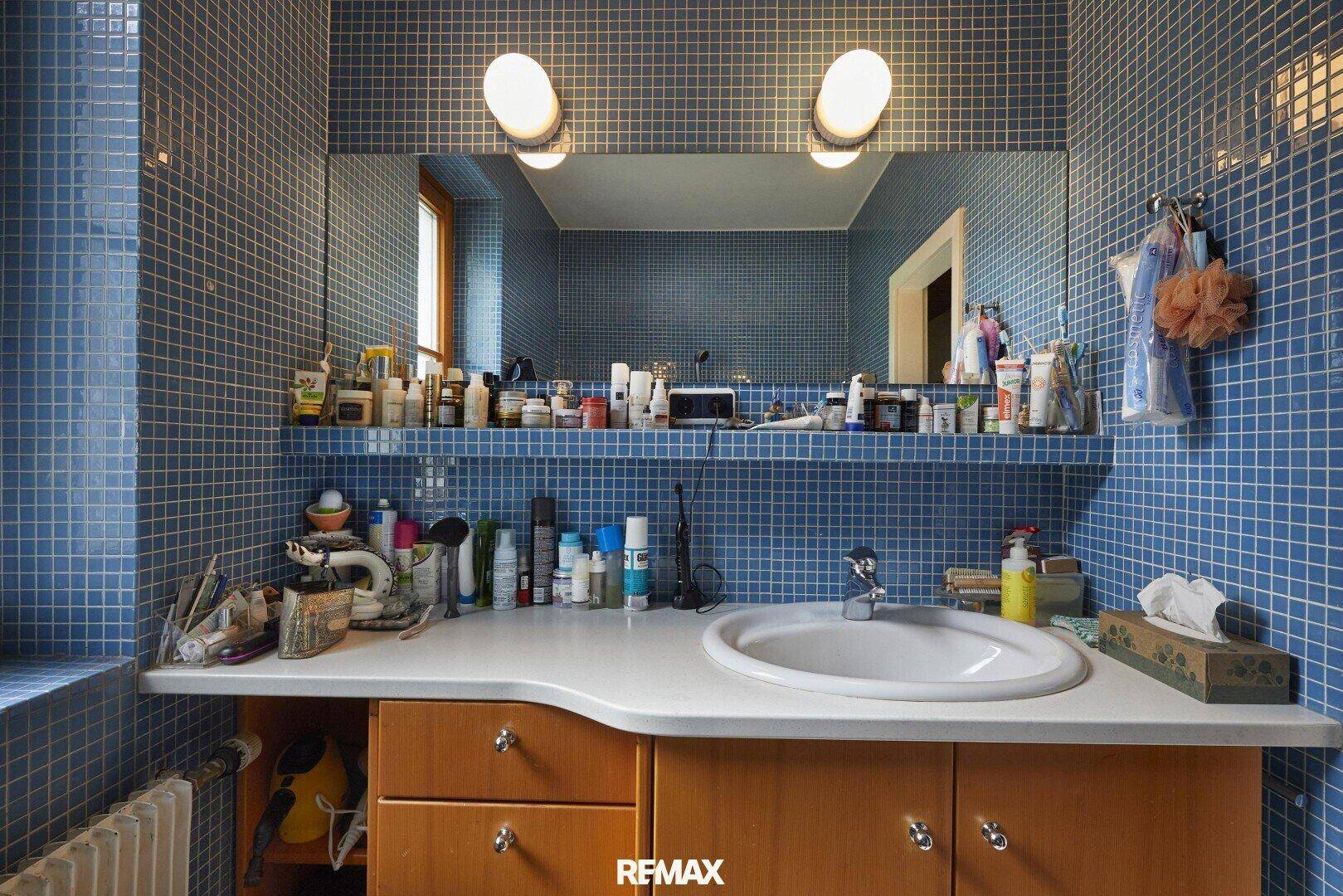 Badezimmer mit blauen Mosaikfliesen, Einzelwaschbecken, großem Spiegel und Fenster für Tageslicht.