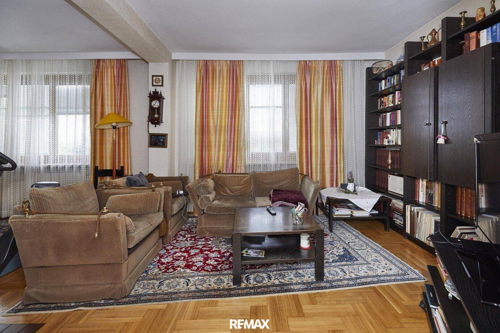 Gemütliches Wohnzimmer mit Parkettboden, bequemen Sofas, Bücherregal und farbenfrohen Vorhängen.