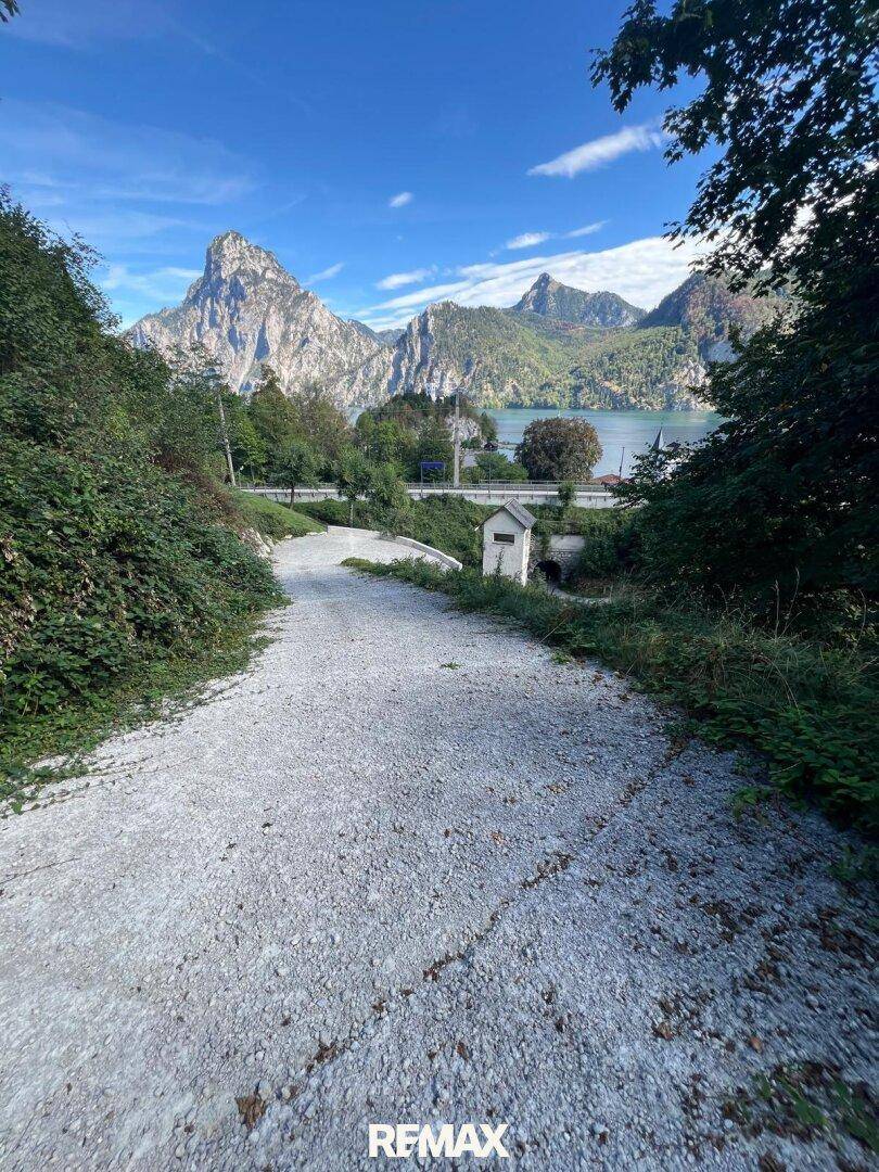 Schotterweg führt zu einem malerischen See mit majestätischen Bergen im Hintergrund.