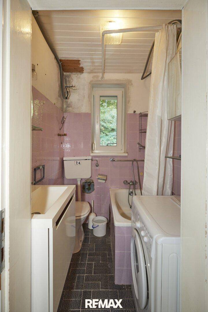 Kleines Badezimmer mit rosa Fliesen, Badewanne, Waschbecken und Waschmaschine, mit Fenster zum Garten.