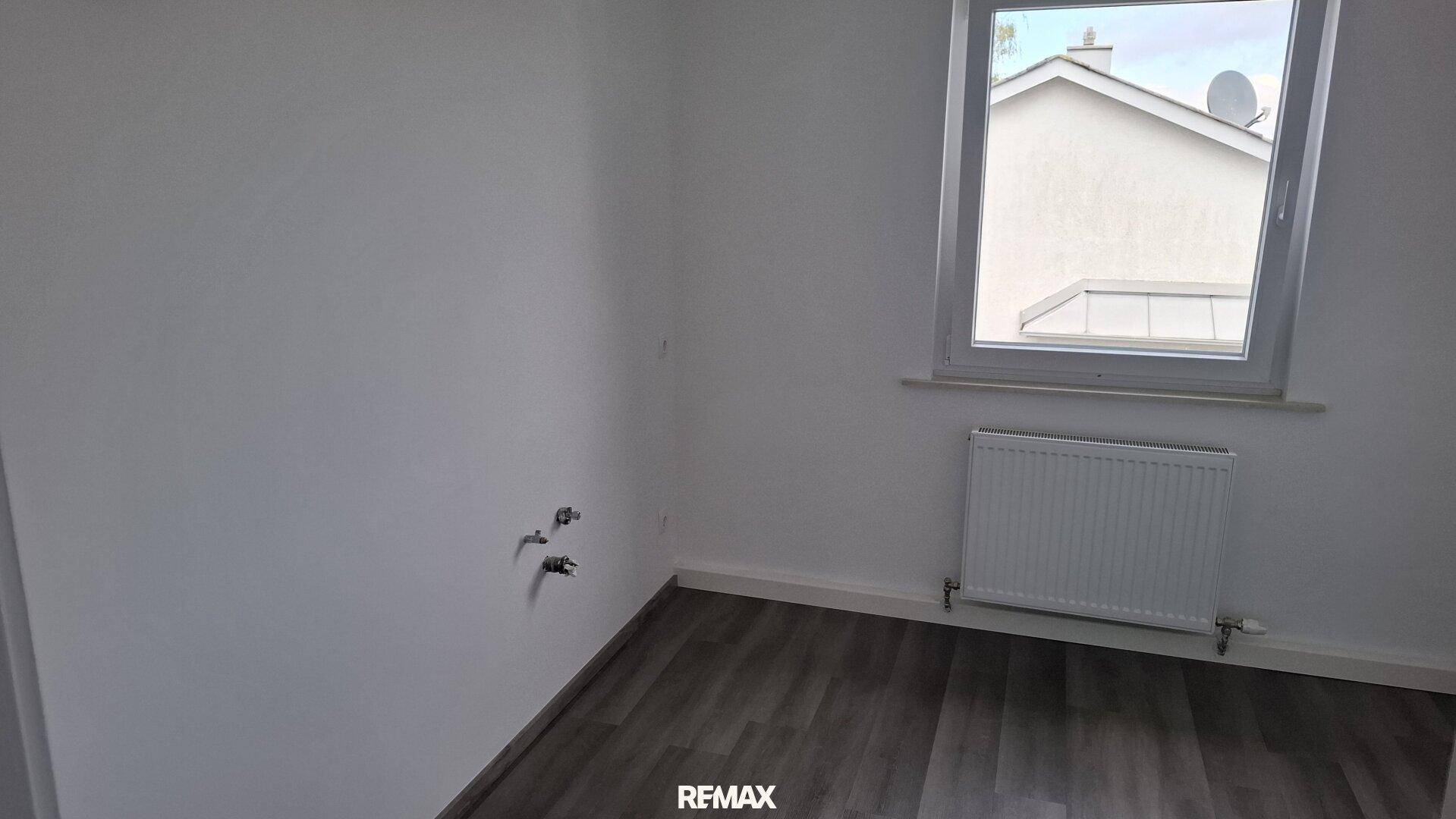 Leerer Raum mit Fenster, Heizkörper und Anschlüssen für eine mögliche Küche oder Bad.