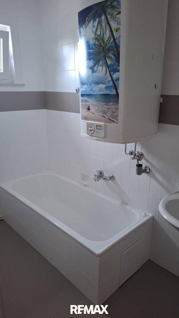 Badezimmer mit Badewanne, weißen Fliesen und Fenster für Tageslicht.