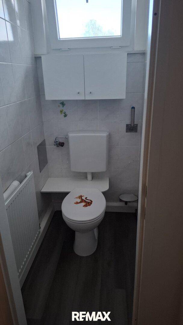 Kleines WC mit Fenster, Toilette und Heizkörper, ausgestattet mit weißen Fliesen.
