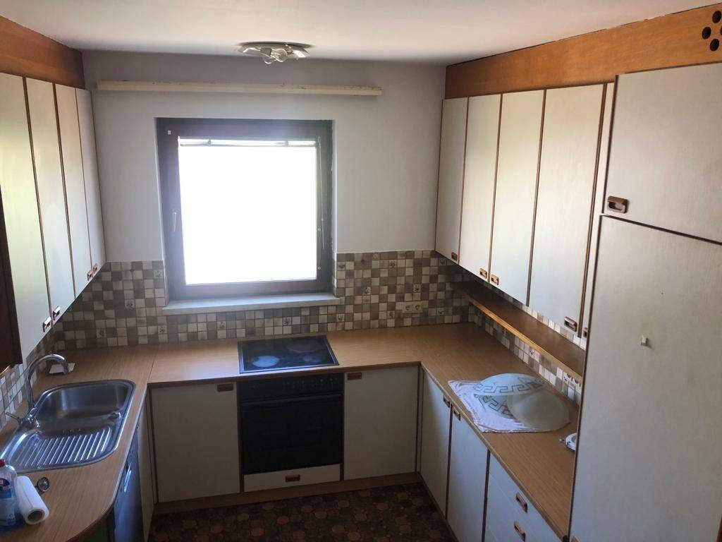 Helle Küche mit Holzfronten, Fliesenrückwand und Fenster.