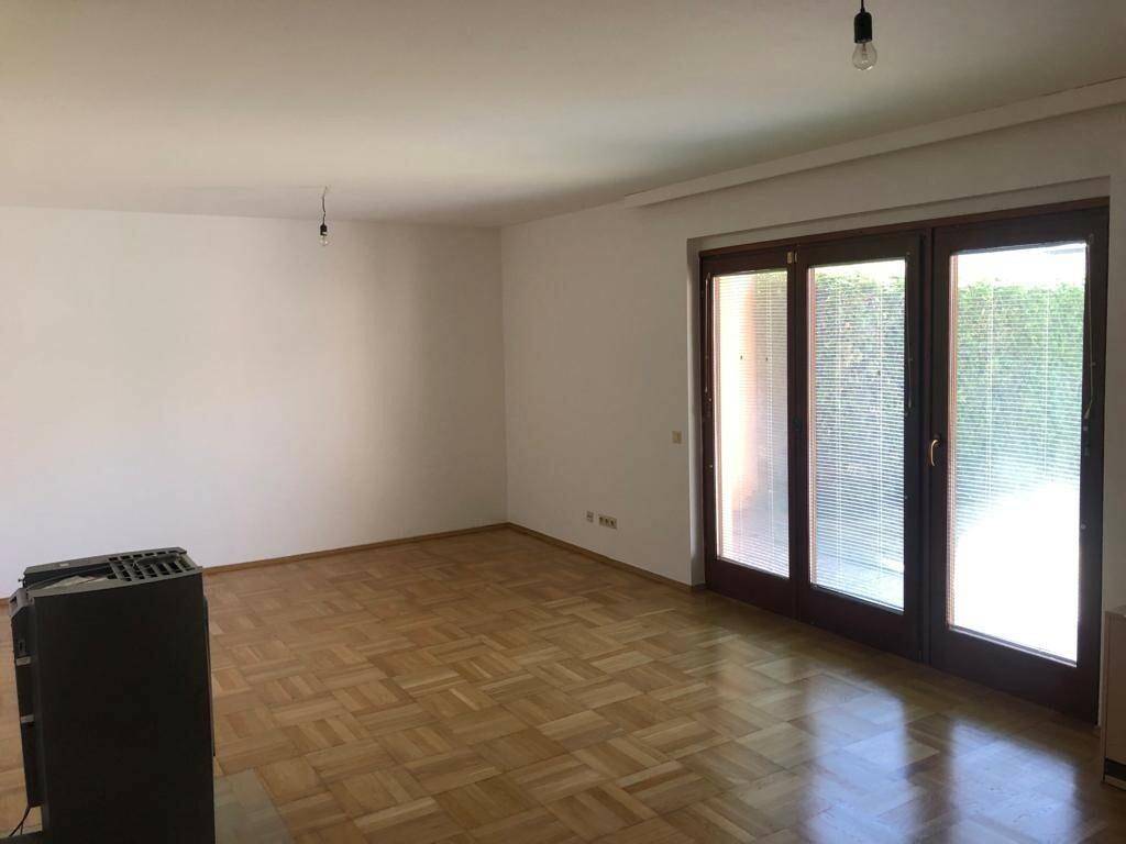 Geräumiges Wohnzimmer mit Parkettboden und großen Fenstertüren zur Terrasse.