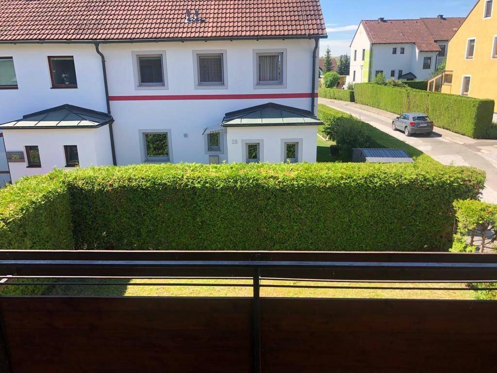 Blick vom Balkon auf die Nachbarhäuser und eine lange, gepflegte Hecke.