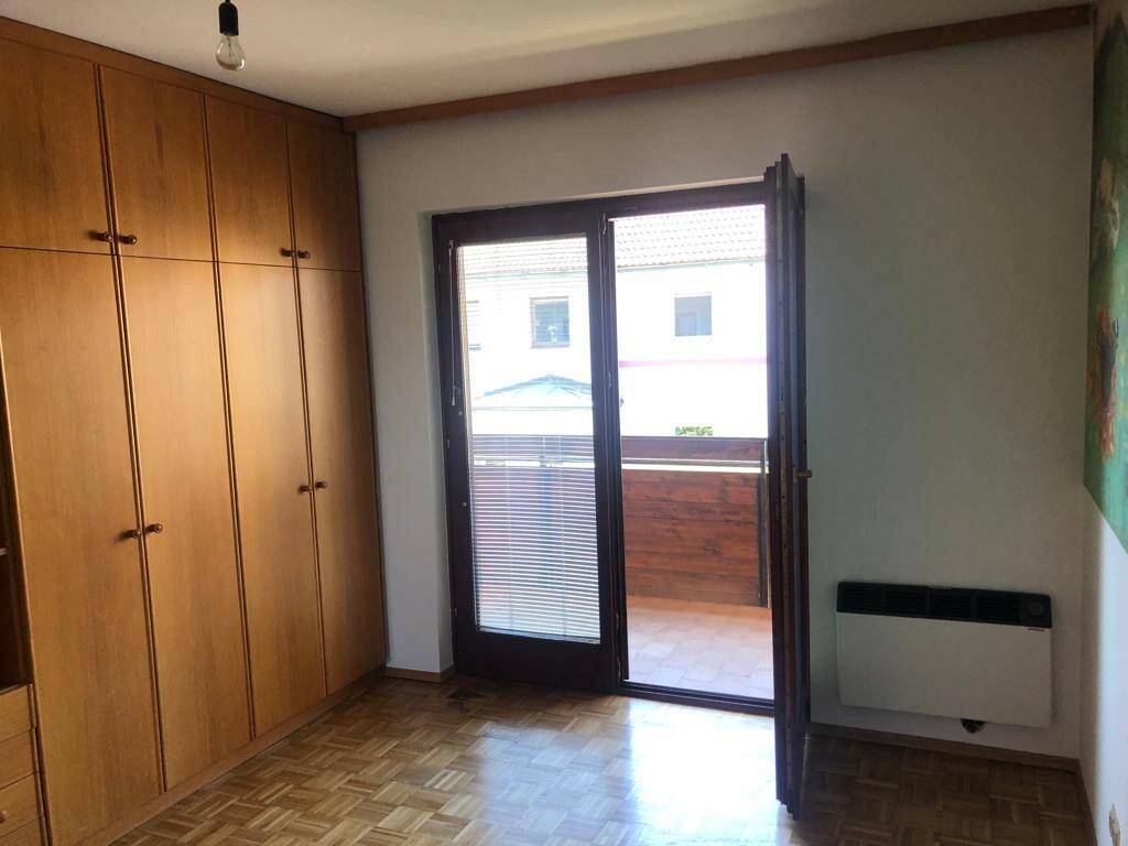 Schlafzimmer mit Parkettboden, Einbauschränken und Zugang zum Balkon.
