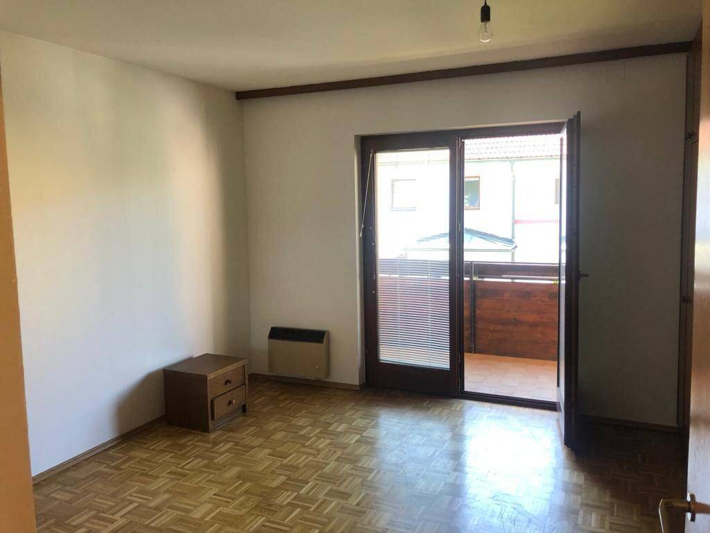 Helles Schlafzimmer mit Parkettboden, Nachttisch und Balkonzugang.