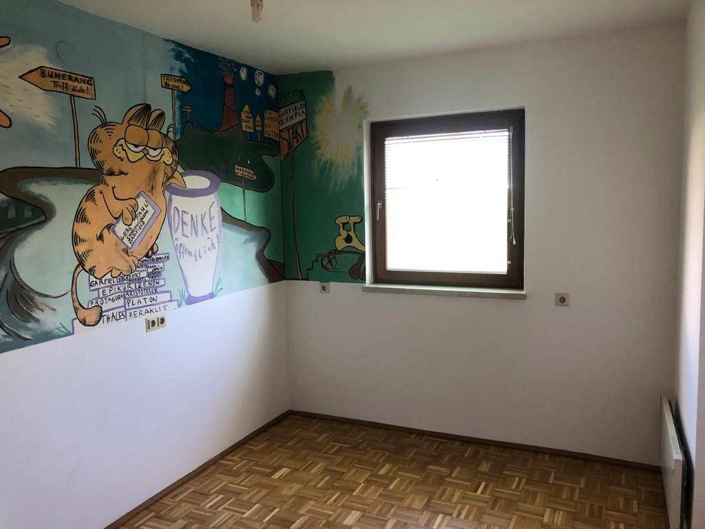 Kinderzimmer mit Parkettboden, Fenster und bunter Wandmalerei.