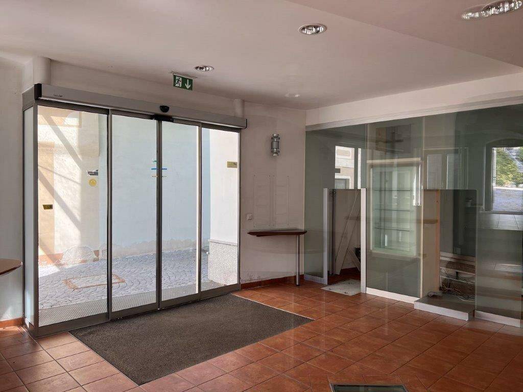 Heller Eingangsbereich mit automatischen Glasschiebetüren und Terrakotta-Fliesenboden.