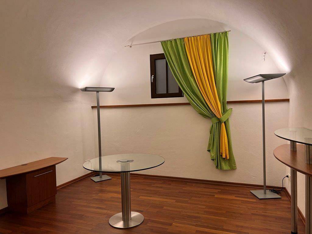 Gemütlicher Raum mit Gewölbedecke, Holzparkett und farbenfrohen Vorhängen, beleuchtet von Stehlampen.