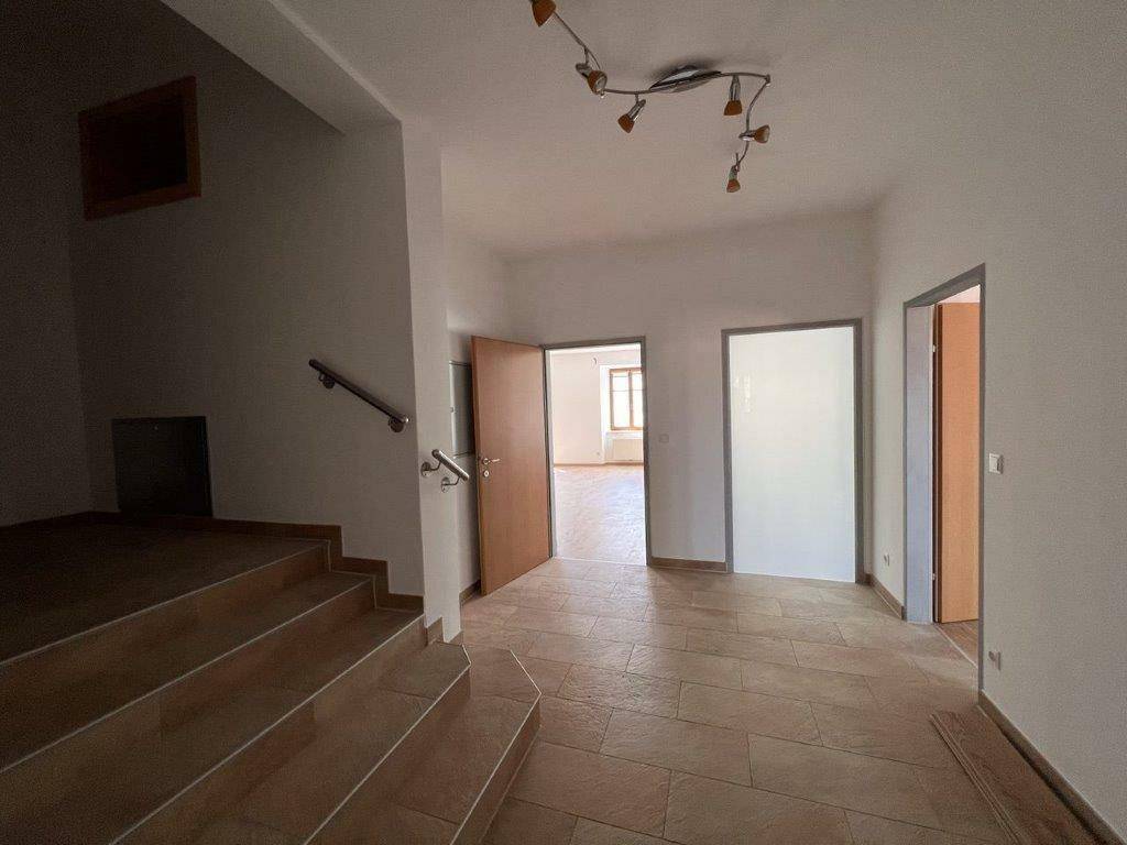 Geräumiger Eingangsbereich mit gefliestem Boden und Holztreppe, führt zu weiteren Räumen.