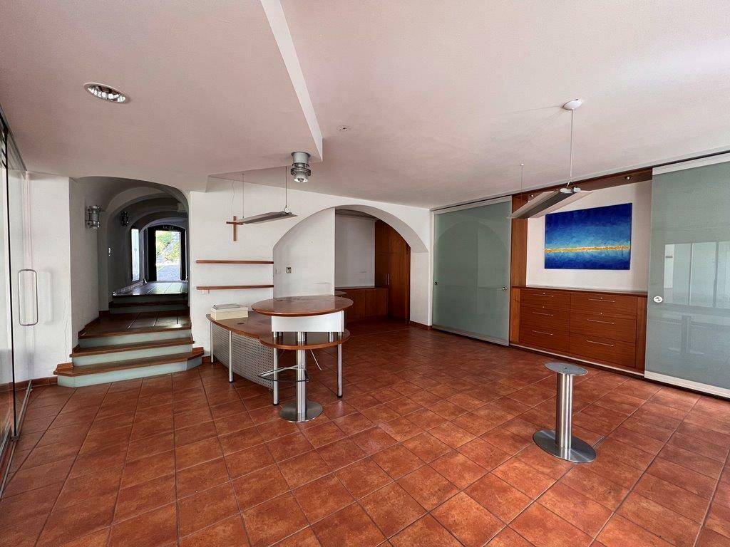 Großer offener Raum mit Terrakotta-Fliesenboden und modernen Möbeln, verbunden mit einem Flur.