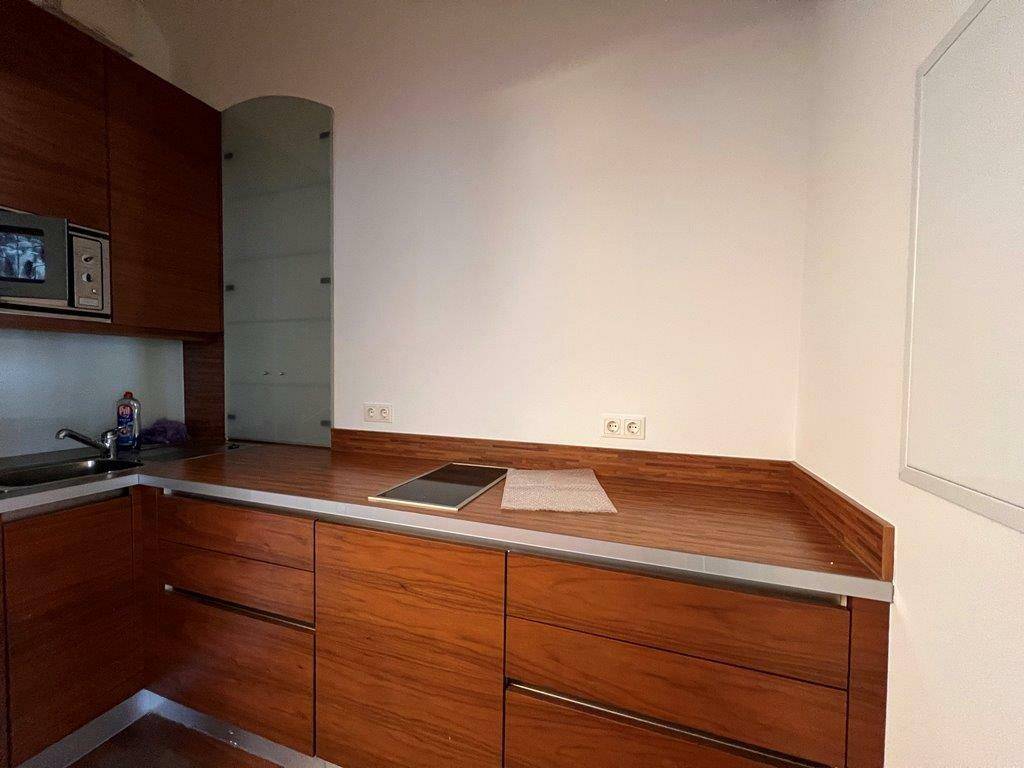 Kleine, moderne Küchenzeile mit Holzfronten, integrierter Mikrowelle und Kochfeld.