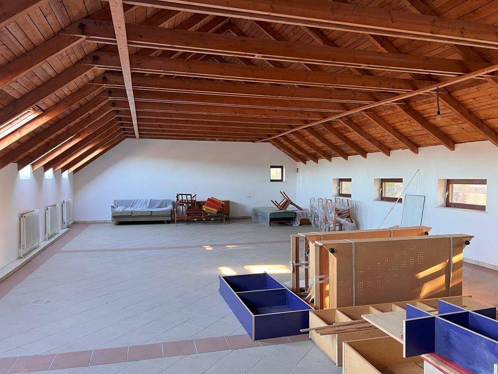 Großer offener Dachboden mit sichtbaren Holzbalken, Fliesenboden und viel Tageslicht.