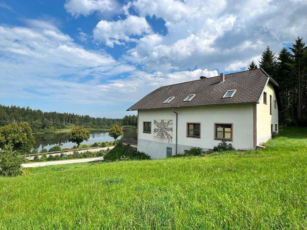 Landhaus mit Blick auf einen See und umliegende Wälder unter strahlend blauem Himmel mit Wolken.