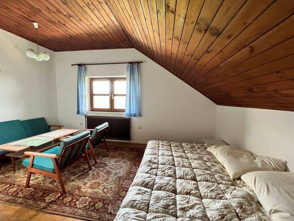 Geräumiges Schlafzimmer im Dachgeschoss mit Holzdecke, Fenster und Sitzgelegenheiten.