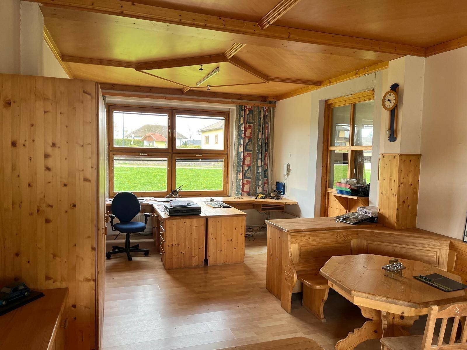 Gemütliches Büro mit viel Holzvertäfelung, Holzboden und großen Fenstern mit Blick ins Grüne.