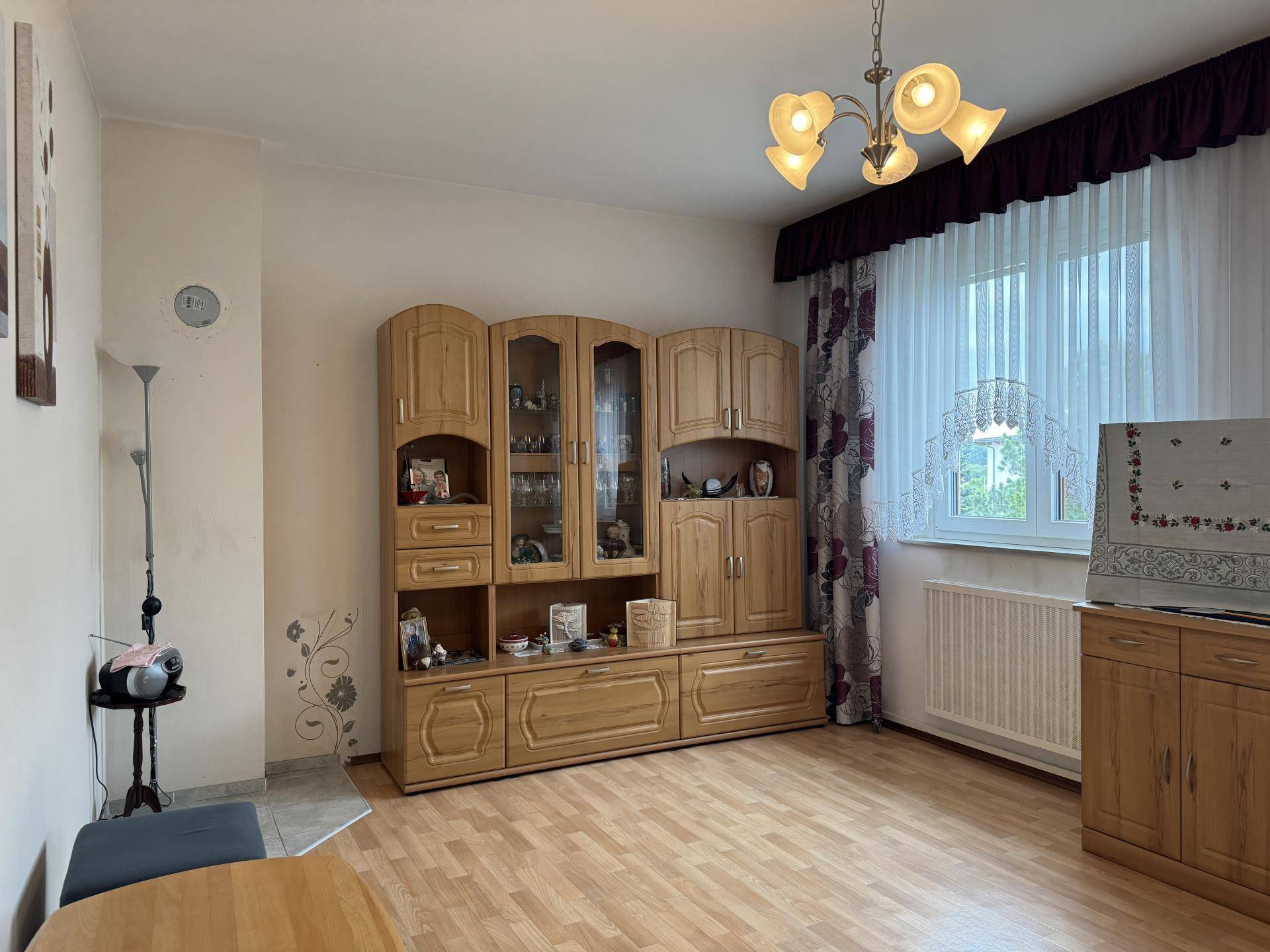 Helles Wohnzimmer mit Laminatboden, Holzschrankwand und großem Fenster.
