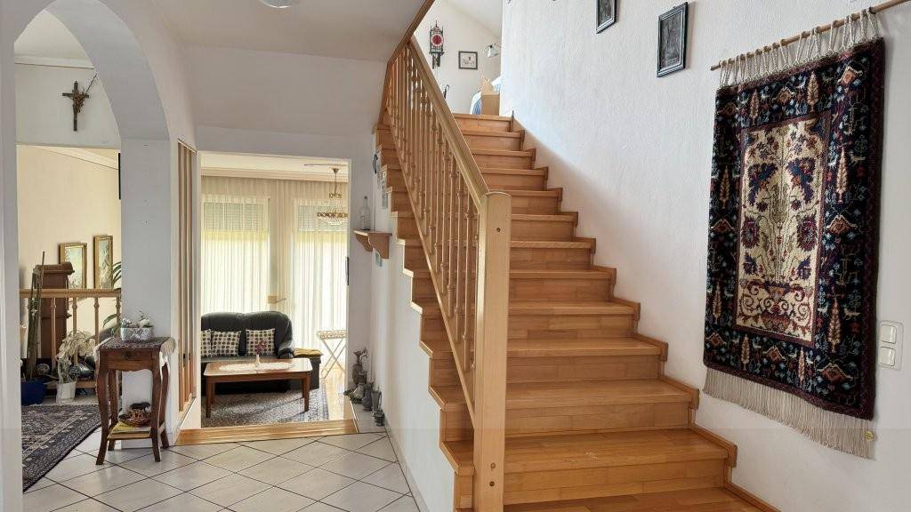 Heller Eingangsbereich mit Holztreppe, Fliesenboden und Zugang zu weiteren Wohnbereichen.