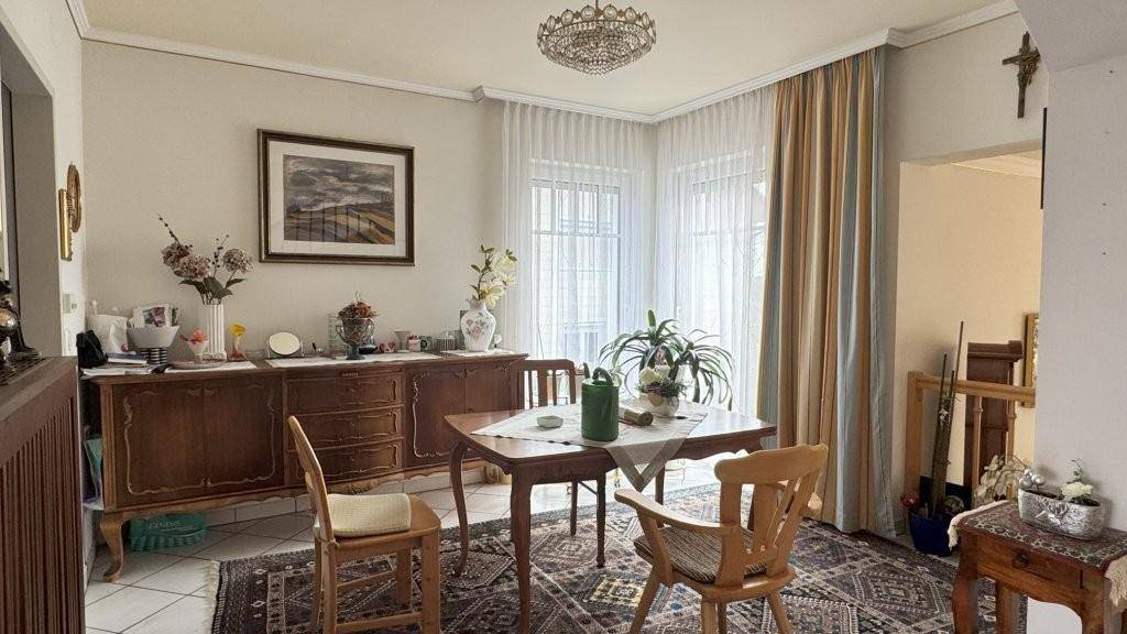Gemütlicher Essbereich mit Holztisch, Stühlen und einem Sideboard, beleuchtet durch große Fenster.