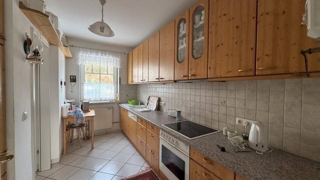 Funktionale Küche mit Holzschränken, Fliesenboden und Fenster mit Blick ins Grüne.