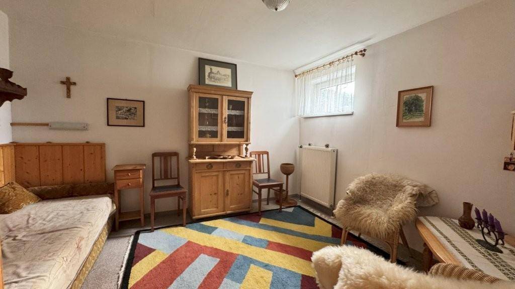 Helles Schlafzimmer mit Einzelbett, Holzmöbeln und einem farbenfrohen Teppich, gemütlich eingerichtet.