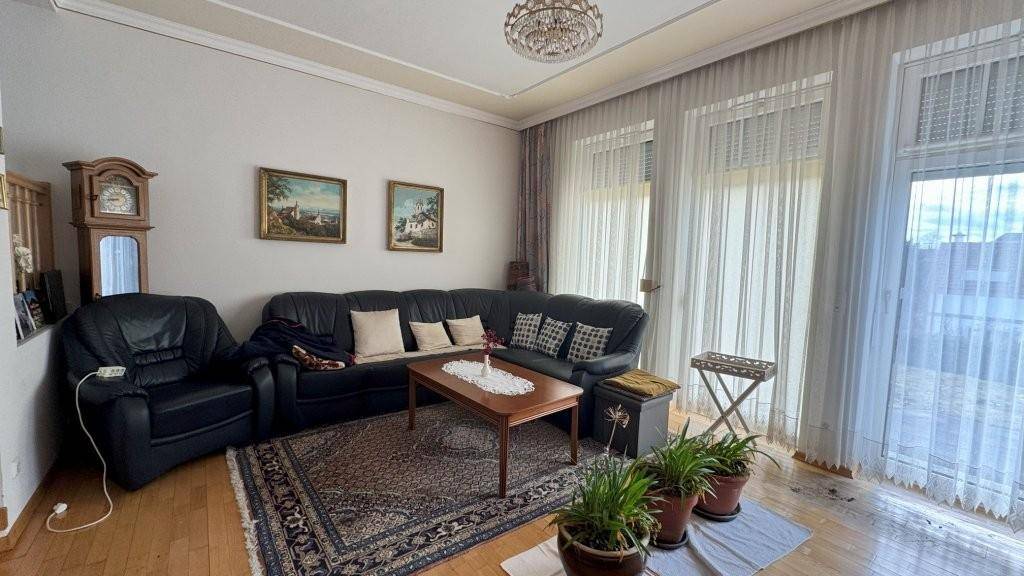 Geräumiges Wohnzimmer mit dunklem Ledersofa, Holzboden und großen Fenstern für viel Licht.