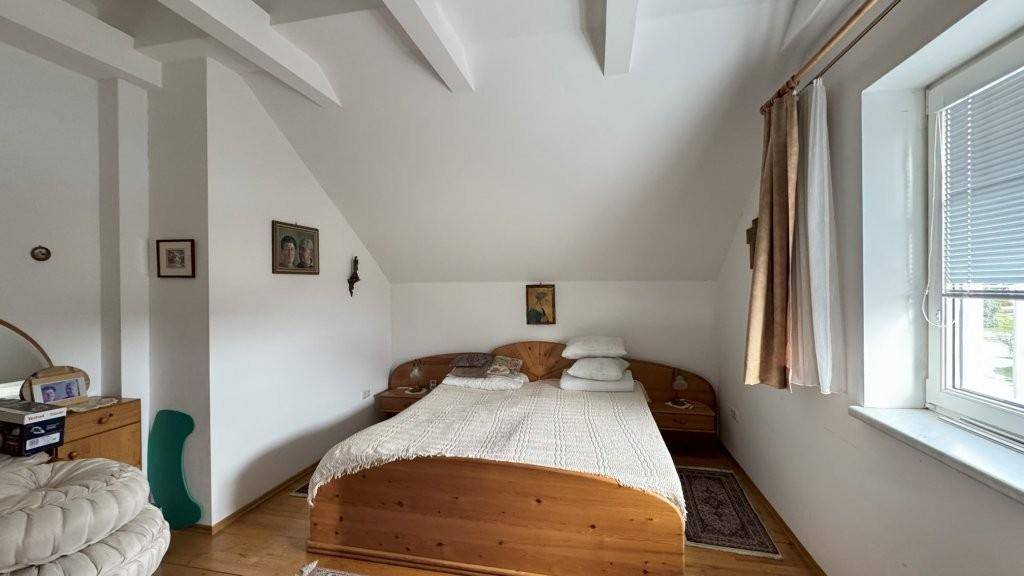 Schlafzimmer im Dachgeschoss mit Holzbett, schrägen Wänden und einem Fenster für Tageslicht.