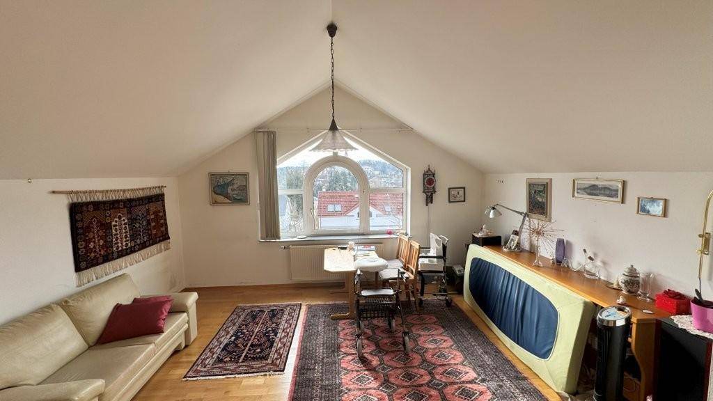 Gemütlicher Dachbodenraum mit schrägen Wänden, Holzboden und einem großen Bogenfenster.